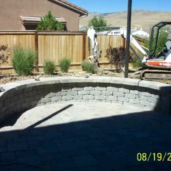 back yard patio with stone wall, wooden fence, and a backhoe.