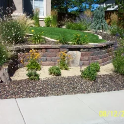 short brick wall with gravel and various plants below a grass yard